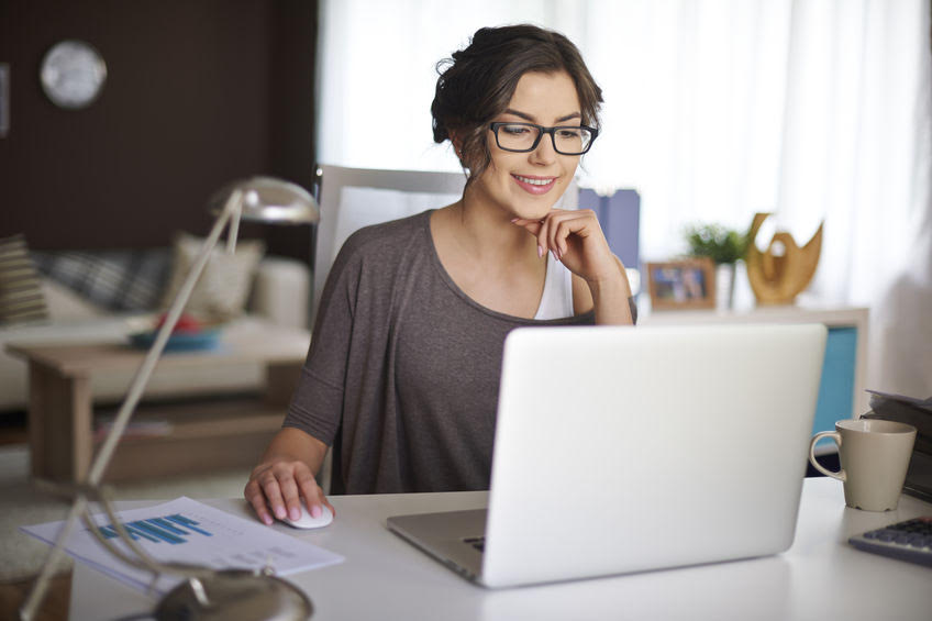 Woman working at a laptop with documents on her desk.